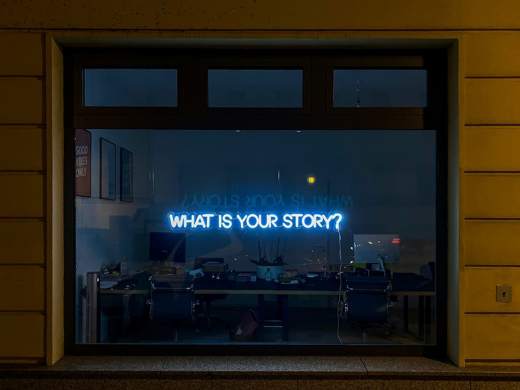 "What is your story" written in blue neon lights in a store window.