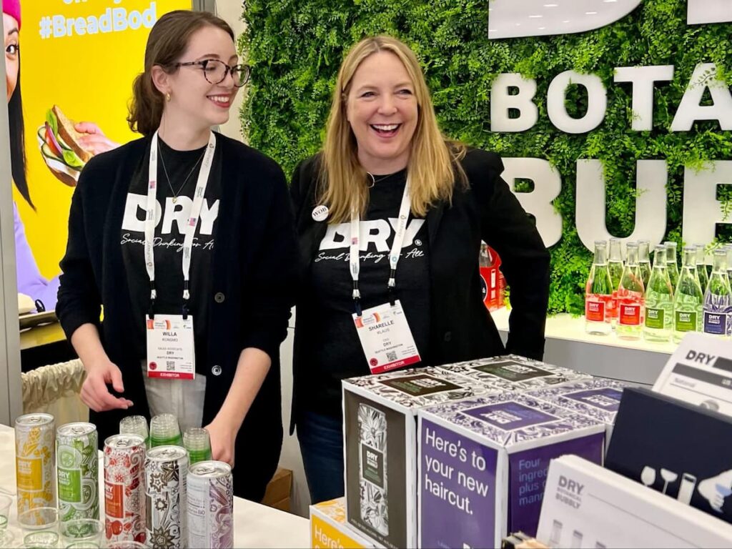 Two women at the Natural Products Expo, handing out samples of a canned beverage.