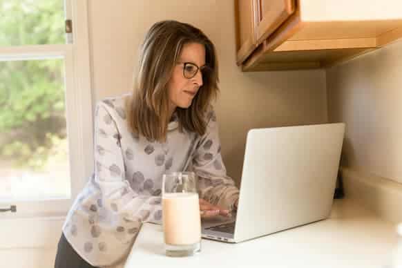 Woman looking at laptop with a glass of milk in the foreground