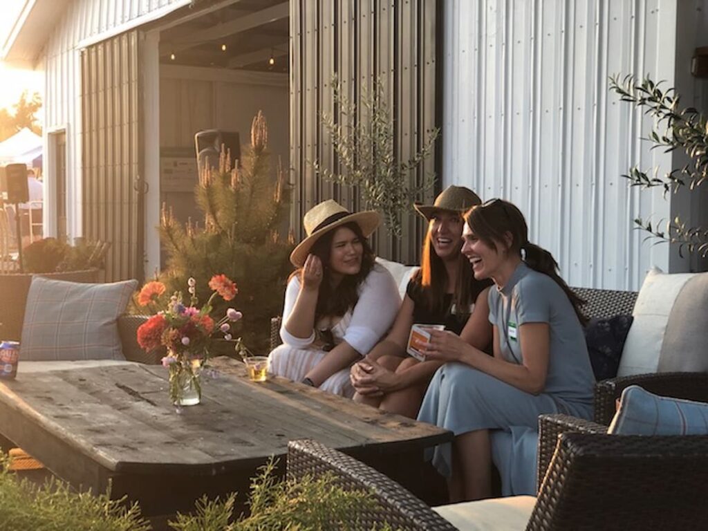 Three women on outdoor couch with drinks.